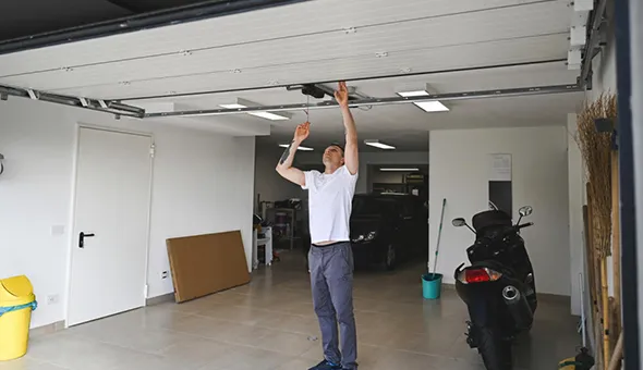 A worker standing inside a garage, raising a garage door.
