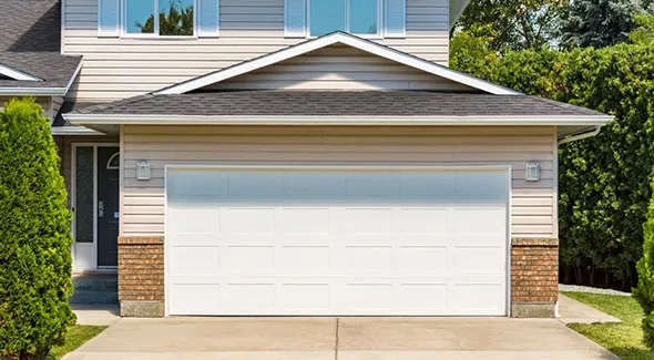 Close-up of a single white garage door on a residential building with a green hedge and clear sky.